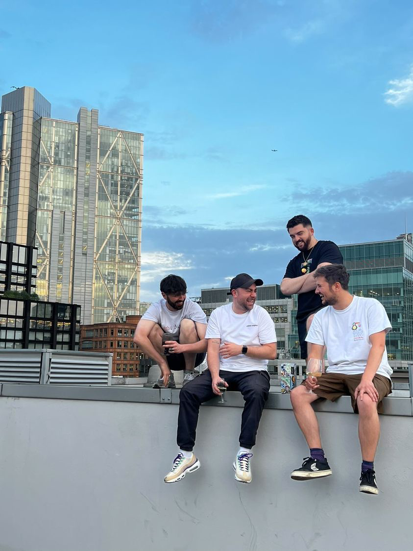 A group of colleagues enjoy a glass of wine sitting on a balcony with a view over London skyscrapers